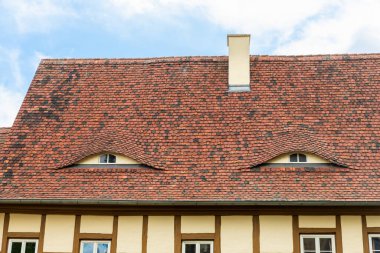 Old beautiful european german fachwerk building rooftop with eye shaped windows and chimney. Typical traditional ancoent house roof architecture in Europe. Funny face-shaped pareidolia facade.