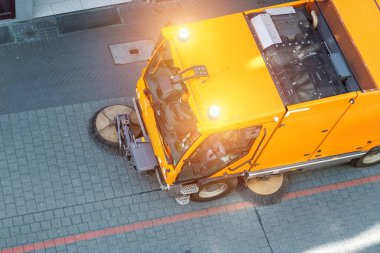 Top above view of small sweeping vacuum cleaner machine equipment removing dust rubbish city street sidewalk paved road near apartment condo building. Special municipal sweeper vehicle cleaning town.
