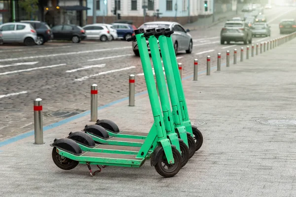 Many modern green electric scooters sharing parked city street. Self-service street transport rental service. Rent urban mobility vehicle with smartphone application. Zero emission green eco energy.