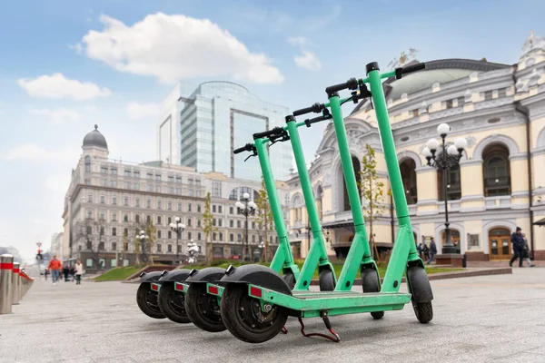 Many modern green electric scooters sharing parked city street. Self-service street transport rental service. Rent urban mobility vehicle with smartphone application. Zero emission green eco energy.