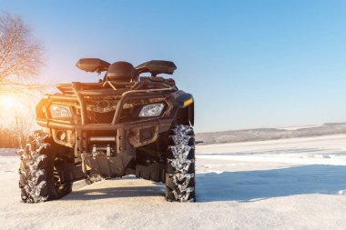 Front POV close-up detail view of quad bike offroad vehicle parked in snowdrift track on sunny snowy cold winter morning against clear blue sky. ATV adventure extreme sport. Nature country tour drive.