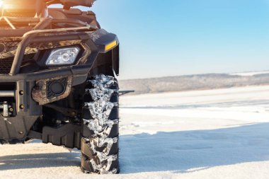 Front POV close-up detail view of quad bike offroad vehicle parked in snowdrift track on sunny snowy cold winter morning against clear blue sky. ATV adventure extreme sport. Nature country tour drive.