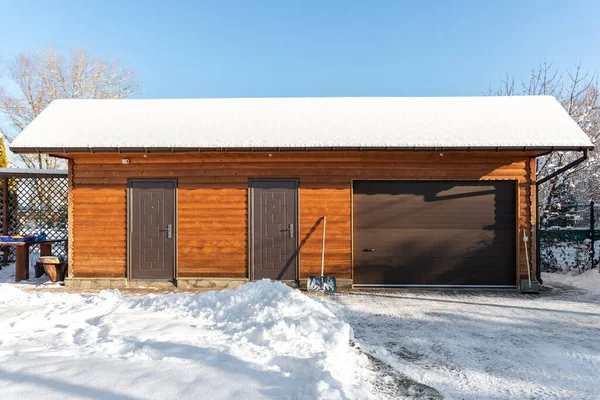 Facade front wall view closed door ATV home garage workshop clutter shed storage warehouse building snowy winter day. House organized warehouse tools equipment. Snow clean removal cold sunny weather.