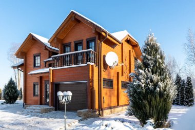 Scenery facade front view of modern wooden luxury timber eco house villa with garage door snowcapped by white fresh snow at cold sunny winter day. Real estate building construction project exterior.