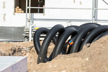 Siyah PVC kıvrımlı plastik yalıtım boruları elektrik kablolarının kablo boruları dezenfekte edilmemiş tesiste. Mühendislik boru hattı drenaj teknolojisi olan yeni modern inşaat alanı.