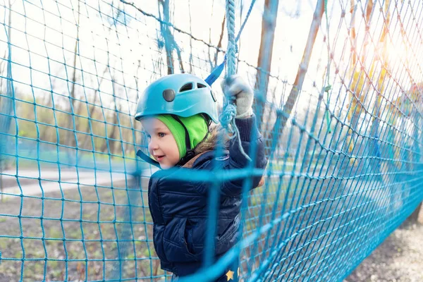 Portrait happy brave courage little toddler child boy wear safety equipment helmet enjoy passing obstacle course forest rope adventure park on cold winter day. Active outside leisure amusement camp.