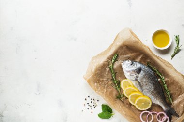 Çiğ Dorado balığı, beyaz bir zemin üzerinde limon, biberiye, soğan, baharat ve yağ dilimleri ile pişirmek için hazırlandı. Üst Manzara. Boşluğu kopyala.