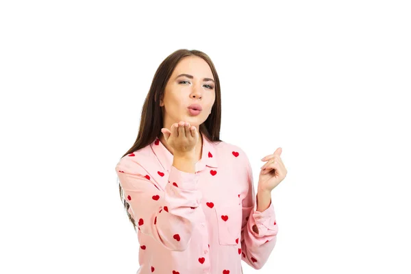 Una chica joven con una camisa rosa con corazones envía un beso de aire. Aislado sobre un fondo blanco. — Foto de Stock