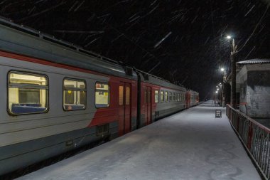 Akşamları yoğun kar altında demiryolu platformunda elektrikli tren.