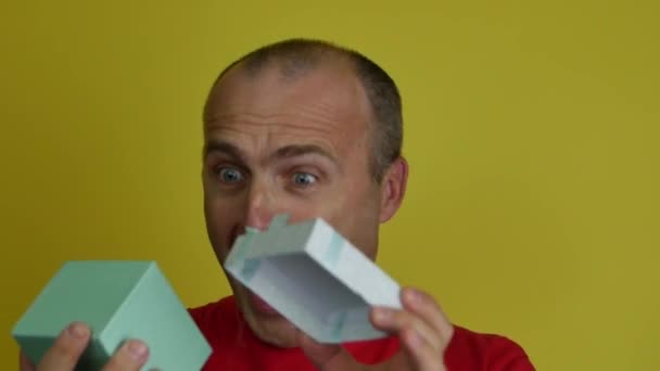 Een man van 40-55 jaar in een rood T-shirt houdt een geschenkdoos in zijn hand en schreeuwt van vreugde. — Stockvideo