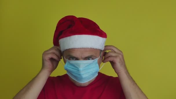 Egy Mikulás sapkás férfi orvosi maszkot visel.. — Stock videók