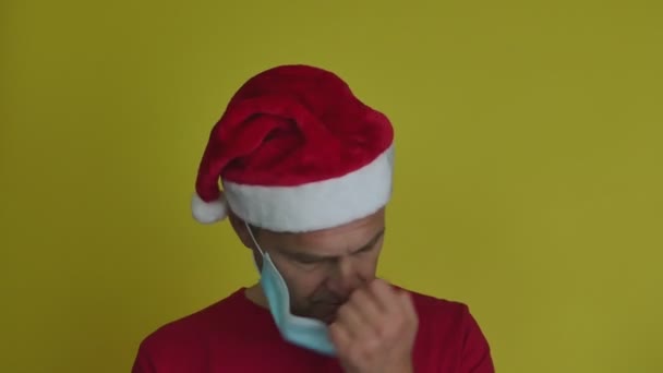 Un uomo con un cappello da Babbo Natale si toglie la maschera medica. — Video Stock