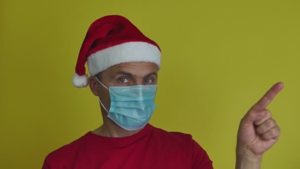 Een man met een kerstmuts en een medisch masker maakt een gebaar met zijn wijsvinger. — Stockvideo