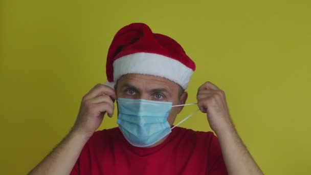 Een man met een kerstmuts doet zijn medisch masker af met opluchting.. — Stockvideo