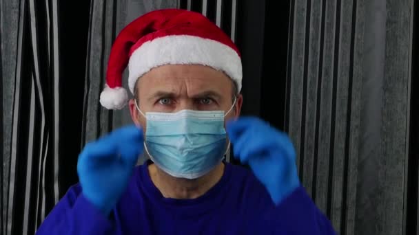 Un hombre con un sombrero de Santa Claus y guantes médicos se quita la máscara médica en alivio. — Vídeo de stock