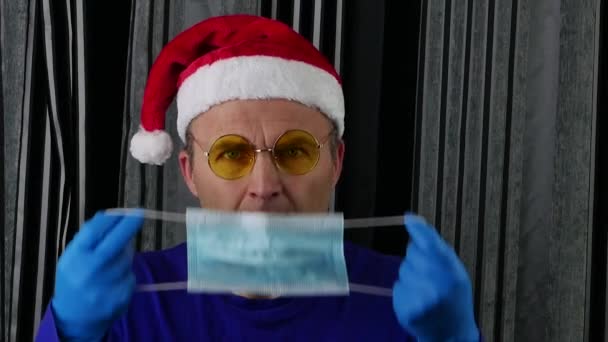 O homem bonito do chapéu de Pai Natal e óculos usa uma máscara médica. — Vídeo de Stock