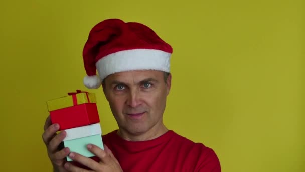 Atrakcyjny mężczyzna 40-50 lat w kapeluszu Mikołaja oferuje pudełka prezentów. — Wideo stockowe