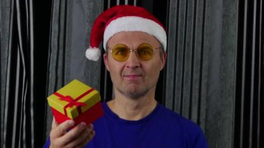 Noel Baba şapkalı ve mavi tişörtlü yakışıklı bir adam elinde bir hediye tutuyor..