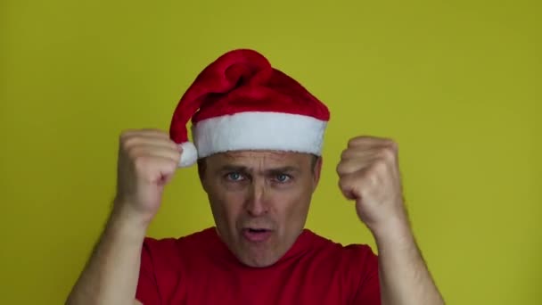 Een knappe man met een kerstmuts drukt zijn emoties uit met handgebaren. — Stockvideo