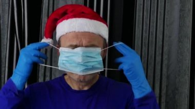 Plastik eldiven takan Noel Baba şapkalı bir adam tıbbi maske takıyor..