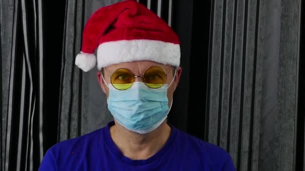 Un hombre con un sombrero de Santa Claus, gafas y guantes médicos se quita la máscara médica.. — Vídeo de stock