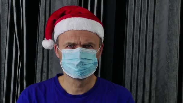 산타 모자를 쓴 남자가 의료 마스크와 장갑을 끼고 손을 벌린다. — 비디오
