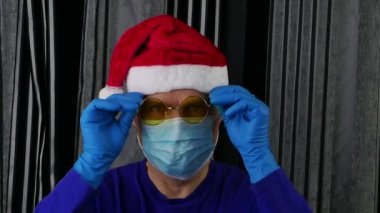 Noel Baba şapkalı ve maskeli bir adam sarı arka planda gözlük takıyor..