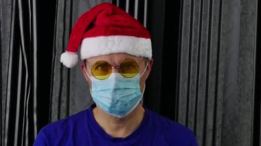Noel Baba şapkalı, gözlüklü ve tıbbi eldivenli neşeli bir adam maskesini çıkarıyor..