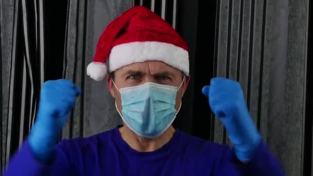 Un uomo con un cappello da Babbo Natale e una maschera medica sta gesticolando con le mani. — Video Stock