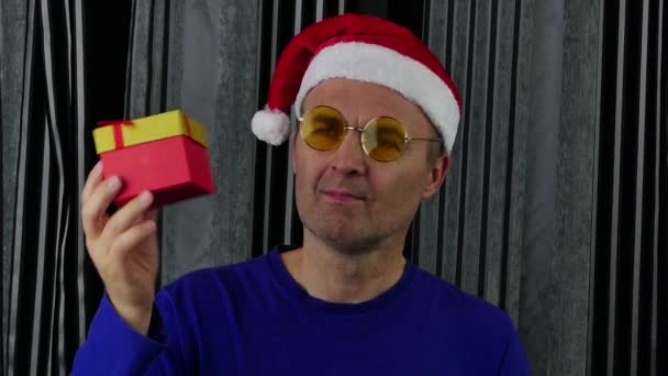 산타 모자를 쓴 남자가 선물 상자를 열고 매우 기뻐 한다. — 비디오