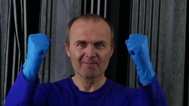 Un hombre con una camiseta azul y guantes de goma gestos con los puños. — Vídeo de stock