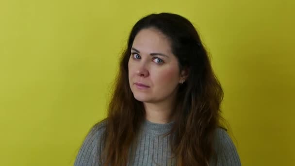 An attractive woman in a gray sweater against a yellow background is surprised and makes a hand gesture. — Vídeo de Stock
