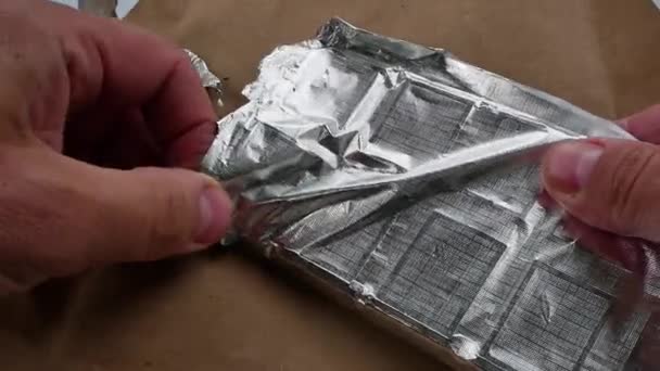 Membongkar kemasan chocalade perak foil di atas meja kayu. — Stok Video