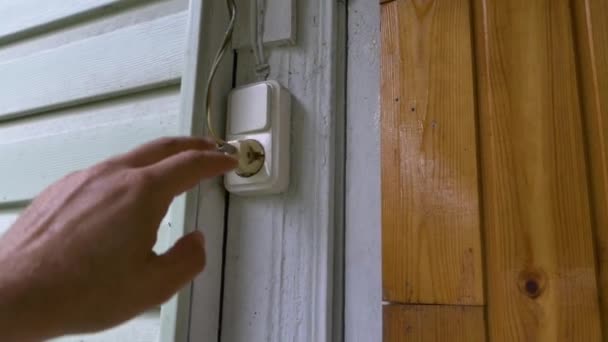 A mans hand pulls out an electrical plug from an outlet on the wall of the house. — Stockvideo