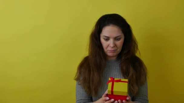 Çekici, neşeli kadın, sarı arka planda bir hediye kutusu tutuyor.. — Stok video
