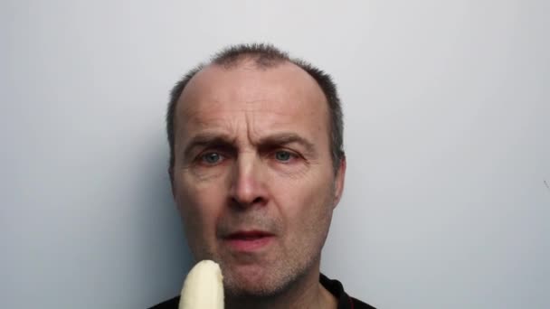 Un homme sur fond blanc mange une banane en gros plan. — Video