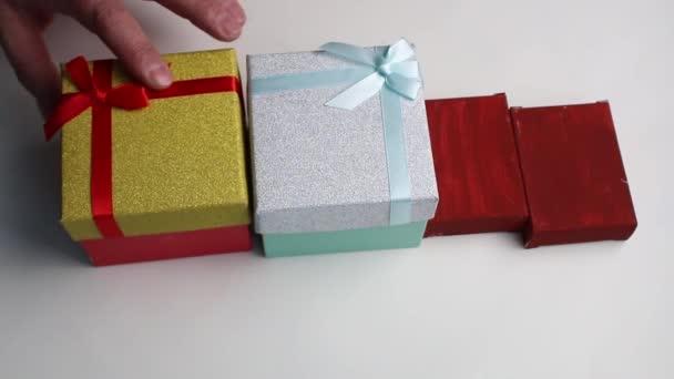 Heren handen nemen op hun beurt drie verschillende gekleurde geschenkdozen op een witte achtergrond. — Stockvideo