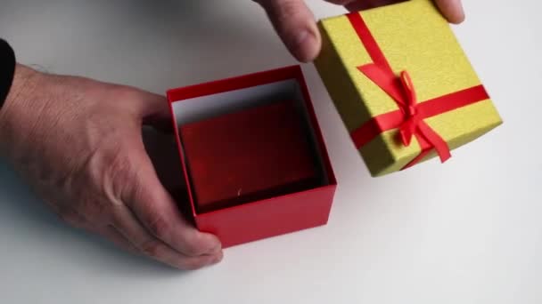 Close-up mannelijke handen halen twee geschenken uit een rood-gele doos. — Stockvideo