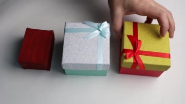 Erkekler sırayla beyaz arka planda üç farklı renkli hediye kutusu alırlar..