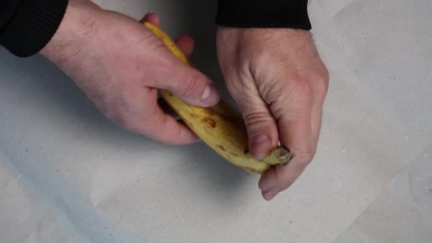 Manliga händer skala en banan på ett papper bakgrund. — Stockvideo