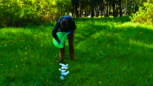 Un adolescent ramasse des déchets en plastique dans les bois sur l'herbe verte. — Video