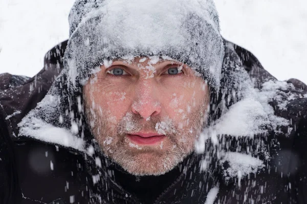 Primer plano de la cara de un hombre helado con un sombrero cubierto de nieve. Fotos de stock