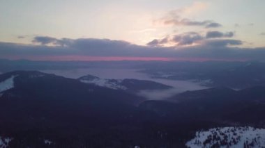 Dağlık bir ormanda, karla kaplı ağaçlarla yükselen güneşin havadan görünüşü.