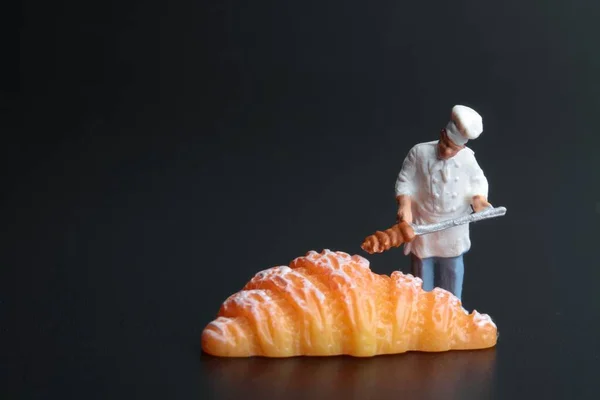 Miniaturfigur Eines Kochs Mit Einem Riesigen Croissant Auf Schwarzem Hintergrund — Stockfoto