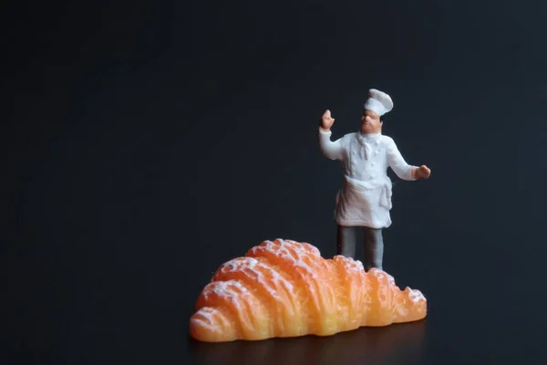 Figurinha Miniatura Cozinheiro Com Croissant Gigante Fundo Preto — Fotografia de Stock