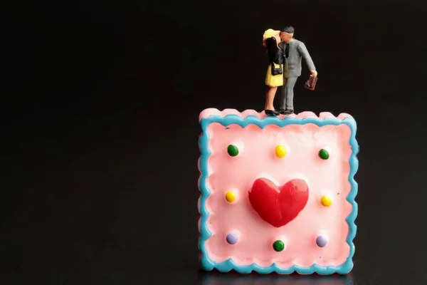 Miniaturfiguren Eines Küssenden Liebespaares Mit Einem Riesigen Dessert Auf Schwarzem — Stockfoto