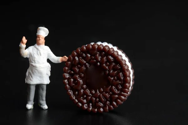 Miniature Figurine Cook Huge Biscuit Black Background — Stockfoto