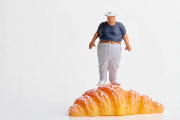 Miniatűr Figura Egy Elhízott Ember Tetején Egy Croissant Fehér Alapon — Stock Fotó