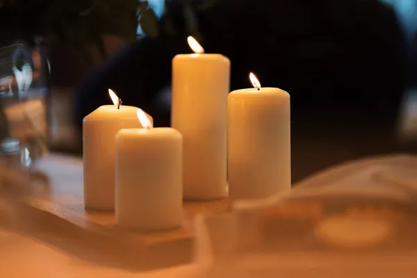 four white candles with a burning wick on a table