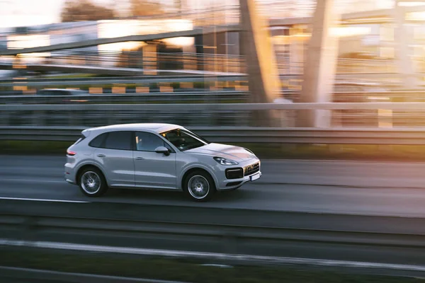 Riga, Letonya - 12 Kasım 2021: Gıcır gıcır spor araba Porsche Cayenne S güneşli bir akşamda yüksek hızda hareket bulanık arka planda bir otoyolda sürüyor